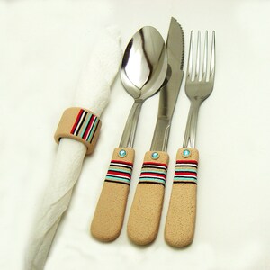May include: Three silver utensils with decorative handles. The handles are beige with red, blue and white stripes. The utensils are a fork, a knife and a spoon.