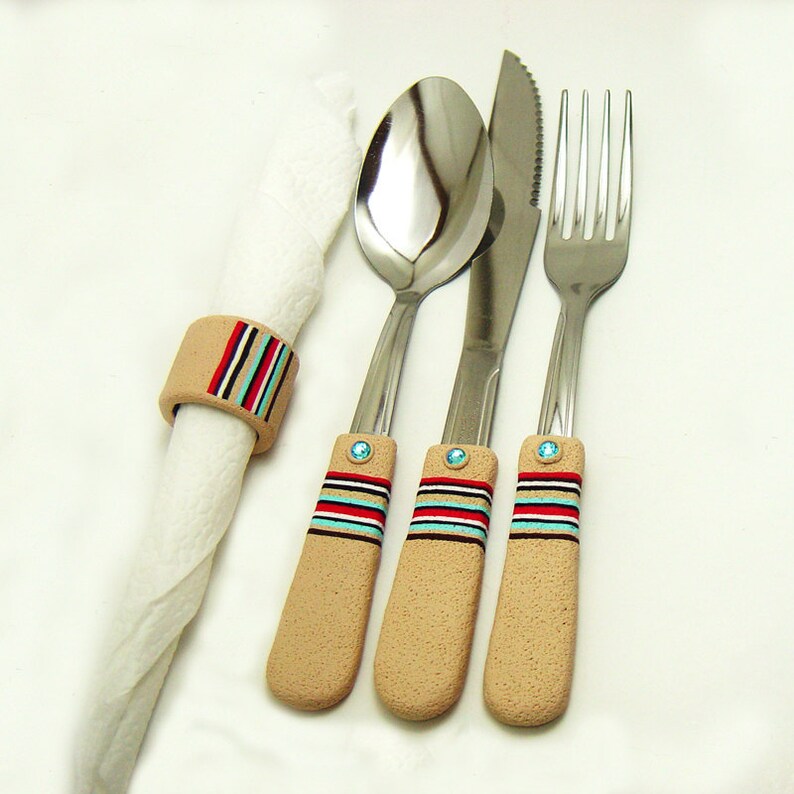 May include: Three silver utensils with decorative handles. The handles are beige with red, blue and white stripes. The utensils are a fork, a knife and a spoon.