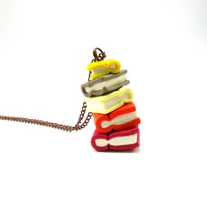 Op de afbeelding: Een ketting met een hanger in de vorm van een stapel van vijf kleurrijke boeken van polymer clay. De boeken zijn gestapeld van klein naar groot, met het bovenste boek geel, gevolgd door grijs, crème, oranje en rood.