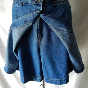 May include: Blue denim shorts with a wrap-around skirt design. The shorts have a button closure and a zipper. The skirt portion wraps around the front and fastens with a button. The denim is a medium wash.