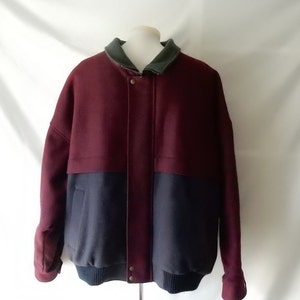 May include: A two-tone jacket in burgundy and navy blue, with a dark green collar. The jacket has a ribbed hem and cuffs, and a button-up front. The jacket is displayed on a mannequin.