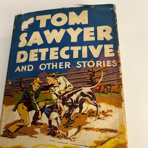 May include: A vintage book cover with a blue background featuring the title "Tom Sawyer Detective and Other Stories" by Mark Twain. The cover art depicts three boys and a dog in a field.