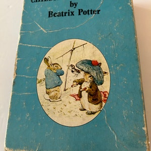 May include: A vintage book titled "CHILDREN'S FAVORITES by Beatrix Potter" with a light blue cover. The cover features a circular illustration of two rabbits and a bird. The book shows signs of wear and tear, with visible creases and discoloration.