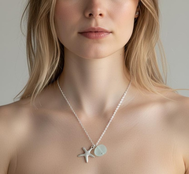 May include: A silver necklace with a starfish and a light blue, round pendant. The necklace is worn around the neck. The starfish charm is detailed and three-dimensional. The pendant is smooth and has a frosted appearance.