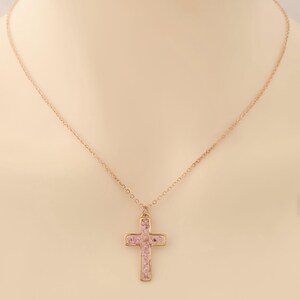 May include: A gold chain necklace with a pink cross pendant. The cross is filled with small pink stones.