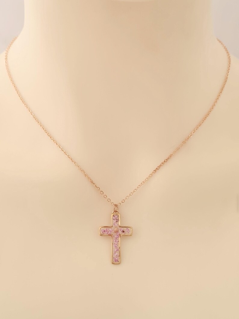 May include: A gold chain necklace with a pink cross pendant. The cross is filled with small pink stones.
