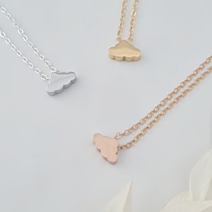 May include: Three delicate cloud-shaped necklaces in silver, gold, and rose gold. The necklaces are on a white background.