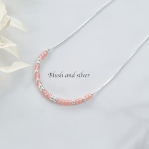 Könnte beinhalten: Eine zarte silberne Kettenkette mit einer Reihe von rosafarbenen und silbernen Perlen. Die Kette liegt auf einem weißen Hintergrund mit dem Text "Blush and silver" darunter.