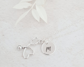 May include: Silver necklace with a stethoscope charm and a round pendant with the letter "M" engraved on it.