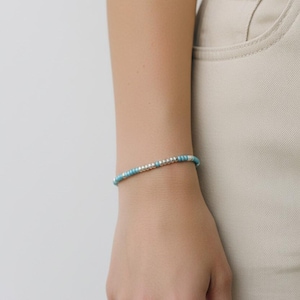 May include: A delicate bracelet with small, round, turquoise and silver beads. The bracelet is worn on a wrist, against a neutral background. The beads are evenly spaced, creating a simple and elegant design.