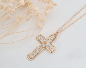 Puede incluir: Collar de cadena dorada con un colgante de cruz. La cruz está llena de flores blancas prensadas.