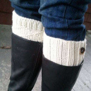 May include: A pair of black leather boots with white knitted leg warmers. The leg warmers have a button on the side.
