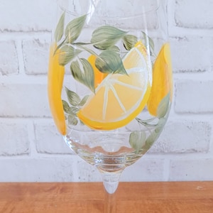 May include: A clear glass wine glass with a hand-painted design of lemon slices and green leaves.