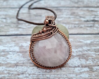 May include: A copper wire wrapped pendant featuring a light pink, cloudy quartz stone. The pendant is attached to a brown leather cord.