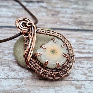 May include: A copper wire wrapped pendant featuring a white agate stone with a green inclusion. The pendant is attached to a brown leather cord.