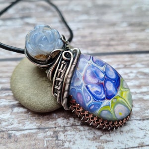 May include: A silver wire wrapped pendant featuring a blue and white carved rose and a blue, purple, green and white marbled stone.