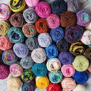 May include: A collection of colorful yarn balls in various shades and patterns. The yarn is arranged in a circular pattern on a light gray surface.