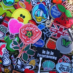 May include: A collection of colorful embroidered iron-on patches featuring various designs, including a rose, a butterfly, a cartoon duck, a heart, a watermelon, a skull, a spider, a seashell, a star, a bone, a mushroom, a  'la la la I'm not listening' patch, a 'New England' patch, a 'Chicago 31' patch, a 'This Way' patch, a 'Don't take away music' patch, a 'Von Bite' patch, a 'One Person Speedwa League' patch, a 'Goldfish Co Vintage' patch, and a 'Freedom Forever' patch.