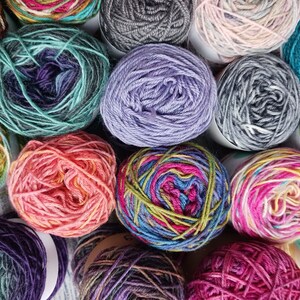 May include: A collection of colorful yarn skeins in various shades of blue, green, purple, pink, red, and brown. The yarn is arranged in a circular pattern, with each skein overlapping the next.