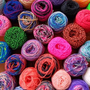 May include: A collection of colorful yarn balls in various shades of pink, blue, green, red, purple, and yellow. The yarn balls are arranged in a random pattern on a wooden surface.
