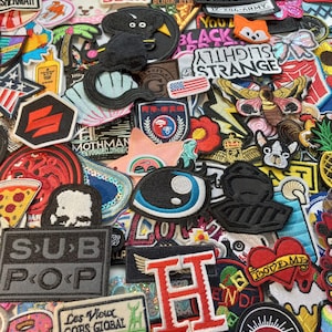 May include: A collection of colourful embroidered iron-on patches featuring various designs, including animals, words, and symbols. The patches are perfect for adding a personal touch to clothing, bags, and other accessories.