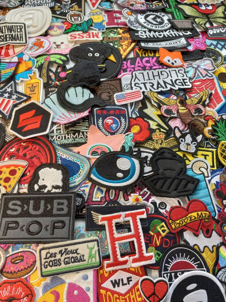May include: A collection of colourful embroidered iron-on patches featuring various designs, including animals, words, and symbols. The patches are perfect for adding a personal touch to clothing, bags, and other accessories.