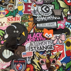 May include: A collection of colourful iron-on patches featuring various designs, including cartoon characters, animals, logos, and text. The patches are arranged in a random pattern on a white background.