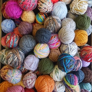 May include: A collection of colorful yarn balls in various shades, including orange, pink, blue, green, and gray. The yarn balls are arranged closely together, creating a textured and vibrant display. Ideal for knitting and crochet projects.