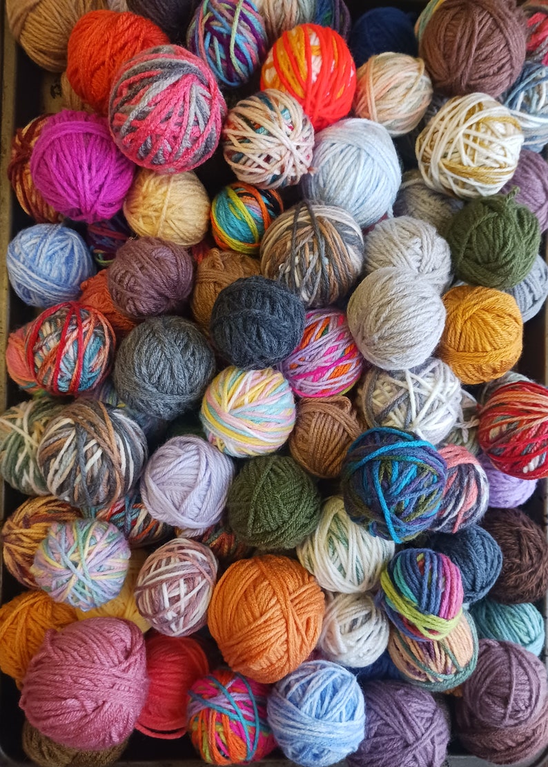 May include: A collection of colorful yarn balls in various shades, including orange, pink, blue, green, and gray. The yarn balls are arranged closely together, creating a textured and vibrant display. Ideal for knitting and crochet projects.