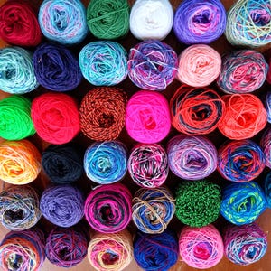 May include: A collection of 40 colorful yarn skeins in various shades of blue, green, red, pink, yellow, and white. The yarn is arranged in a grid pattern.