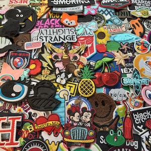 May include: A collection of colourful embroidered iron-on patches featuring various designs, including animals, cartoon characters, words, and symbols. The patches are arranged in a random pattern and are perfect for adding a personalised touch to clothing, bags, or other fabric items.