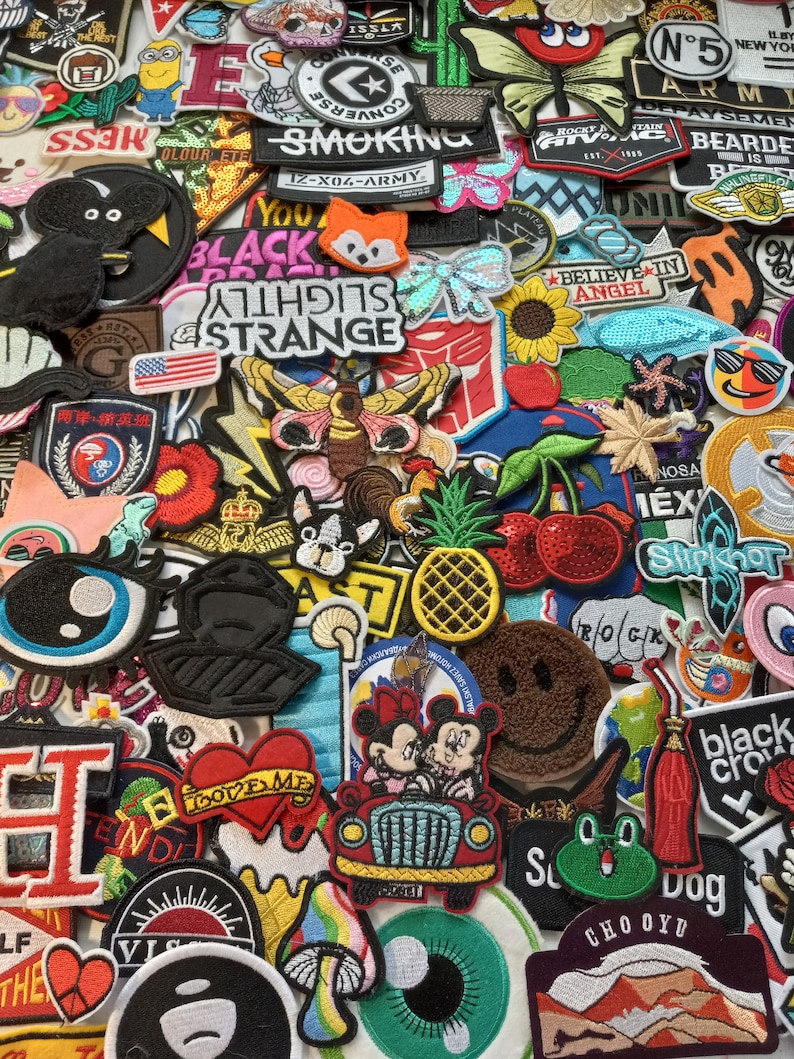 May include: A collection of colourful embroidered iron-on patches featuring various designs, including animals, cartoon characters, words, and symbols. The patches are arranged in a random pattern and are perfect for adding a personalised touch to clothing, bags, or other fabric items.