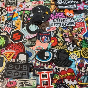 May include: A collection of colourful embroidered iron-on patches featuring various designs, including animals, food, words, and logos. The patches are perfect for adding a personalised touch to clothing, bags, and other accessories.