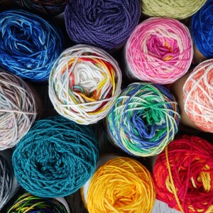 May include: A collection of colorful yarn skeins in various shades of blue, green, red, yellow, pink, white, and gray. The yarn is arranged in a circular pattern, with the ends of the skeins overlapping.