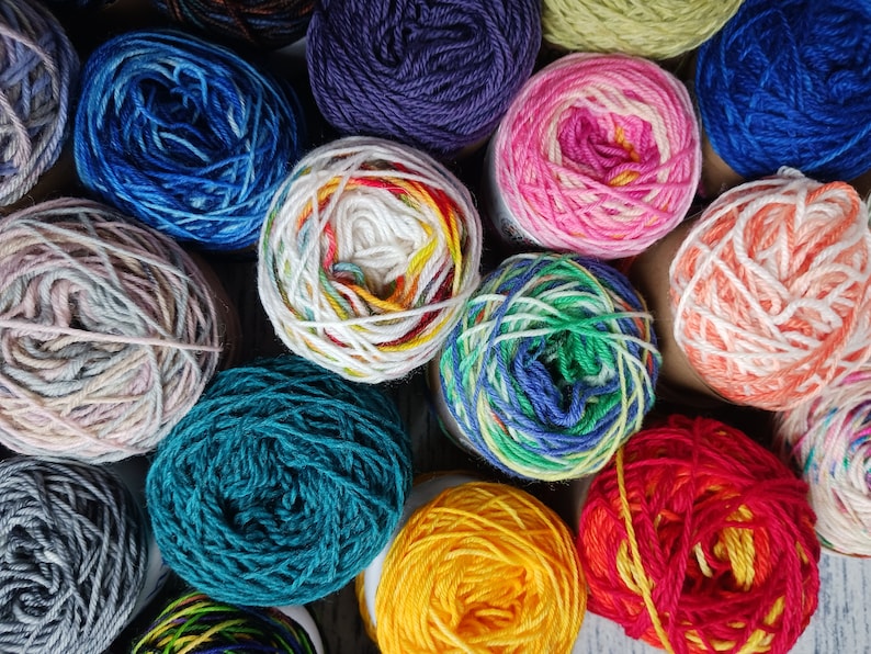 May include: A collection of colorful yarn skeins in various shades of blue, green, red, yellow, pink, white, and gray. The yarn is arranged in a circular pattern, with the ends of the skeins overlapping.