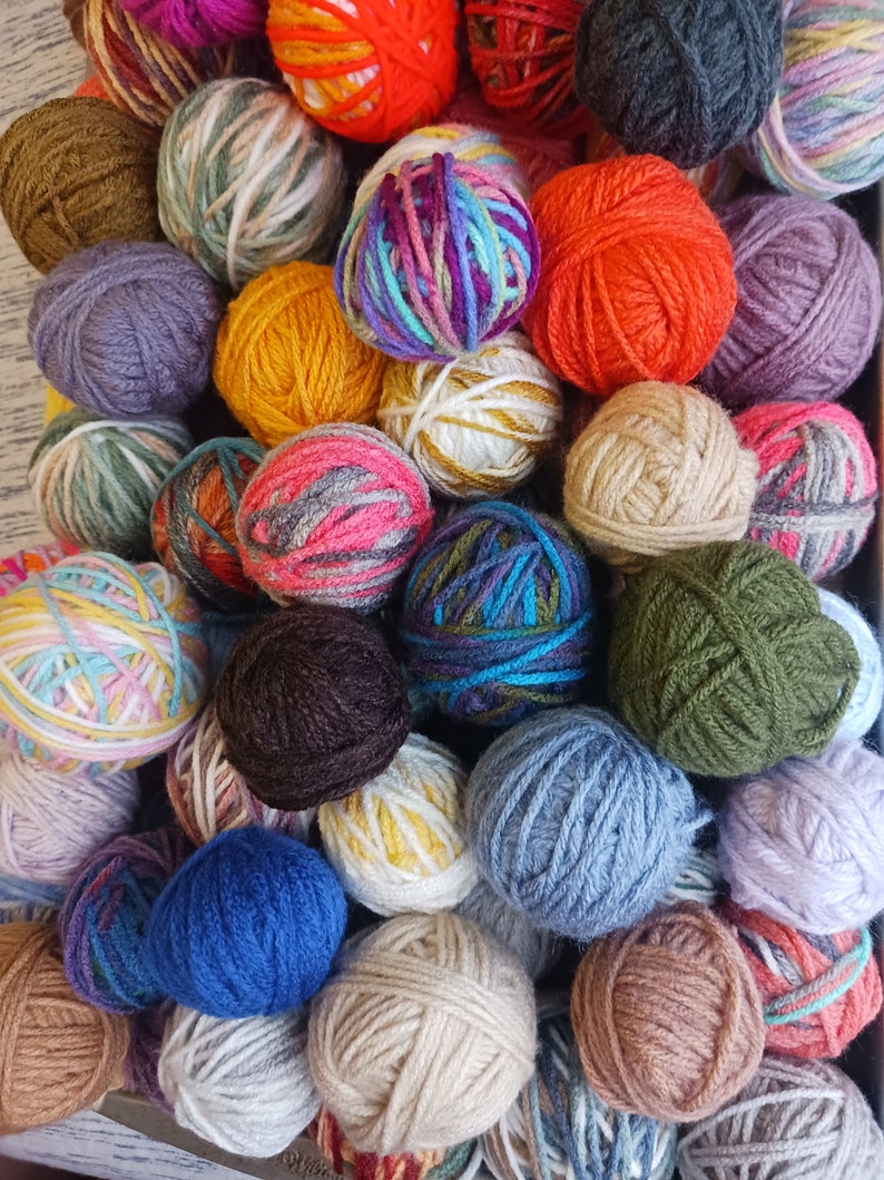 May include: A collection of colorful yarn balls in various shades, including pink, orange, blue, green, and purple. The yarn balls are tightly wound and arranged closely together, creating a textured and vibrant display. Ideal for knitting and crochet projects.