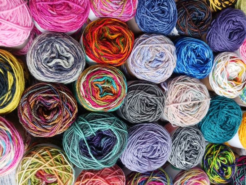 May include: A collection of colorful yarn skeins in various patterns and textures. The yarn is arranged in a circular pattern, with each skein touching the others. The yarn is a mix of bright and muted colors, including red, blue, green, yellow, and purple.