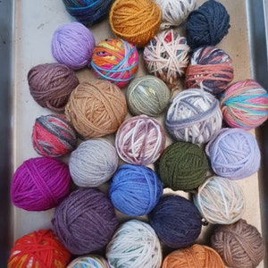 May include: A collection of colorful yarn balls in various shades of blue, purple, green, orange, and brown. The text "EXAMPLE OF 1 POUND" is at the bottom. These yarn balls are ideal for knitting and crocheting projects.