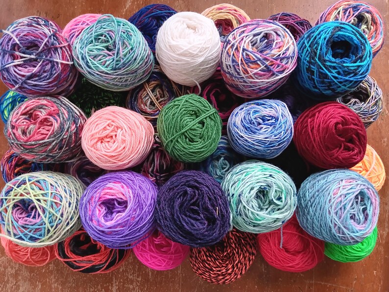 May include: A collection of colorful yarn balls in various shades of blue, green, pink, red, and white. The yarn is arranged in a circular pattern on a wooden surface.