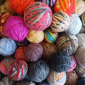 May include: A collection of colorful yarn balls in various shades of orange, pink, purple, blue, and green. The yarn balls are tightly wound and appear to be made of wool or a similar fiber, perfect for knitting or crocheting projects.