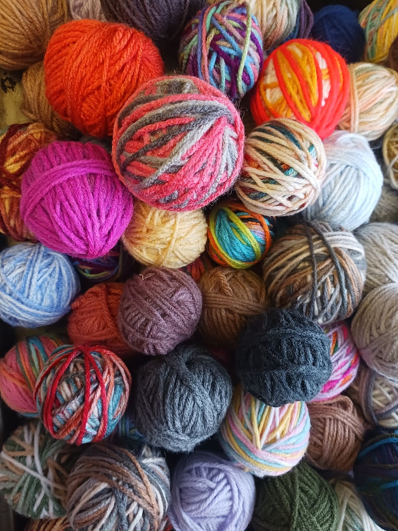 May include: A collection of colorful yarn balls in various shades of orange, pink, purple, blue, and green. The yarn balls are tightly wound and appear to be made of wool or a similar fiber, perfect for knitting or crocheting projects.