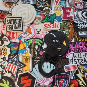 May include: A collection of colourful embroidered iron-on patches featuring various designs, including a cartoon mouse, a palm tree, a seashell, a star, a minion, a military patch, a 'Saltwater Fisherman' logo, and a 'Pancoat' logo.