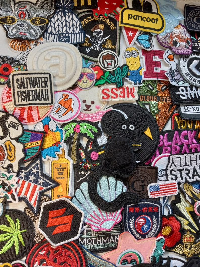 May include: A collection of colourful embroidered iron-on patches featuring various designs, including a cartoon mouse, a palm tree, a seashell, a star, a minion, a military patch, a 'Saltwater Fisherman' logo, and a 'Pancoat' logo.