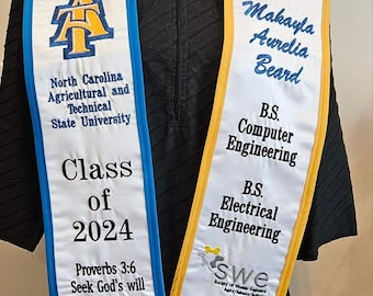 May include: White graduation sash with blue and gold trim. Features the North Carolina A&T State University logo, the text "Class of 2024", and a Bible verse. The other sash has a name, degree information, and SWE leadership titles.