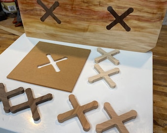 Peut inclure: Une grande dalle de bois non finie avec deux formes de X sculptées. Plusieurs formes de X en bois de différentes nuances de brun et de beige sont disposées sur une surface blanche, ainsi qu'un gabarit en carton. Le bois présente des variations naturelles de grain et de couleur.