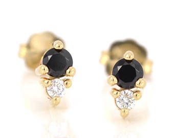 Könnte beinhalten: Ein Paar goldene Ohrringe mit einem schwarzen und weißen Edelstein-Design. Jeder Ohrring hat einen kleinen schwarzen Edelstein, der von einem größeren weißen Edelstein umgeben ist.