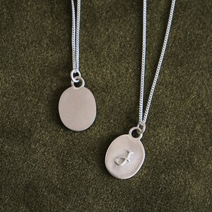May include: Two silver necklaces with oval pendants. One pendant is plain and the other has the letter "J" engraved on it.