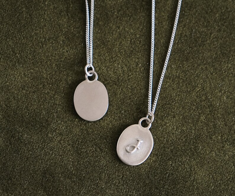 May include: Two silver necklaces with oval pendants. One pendant is plain and the other has the letter "J" engraved on it.
