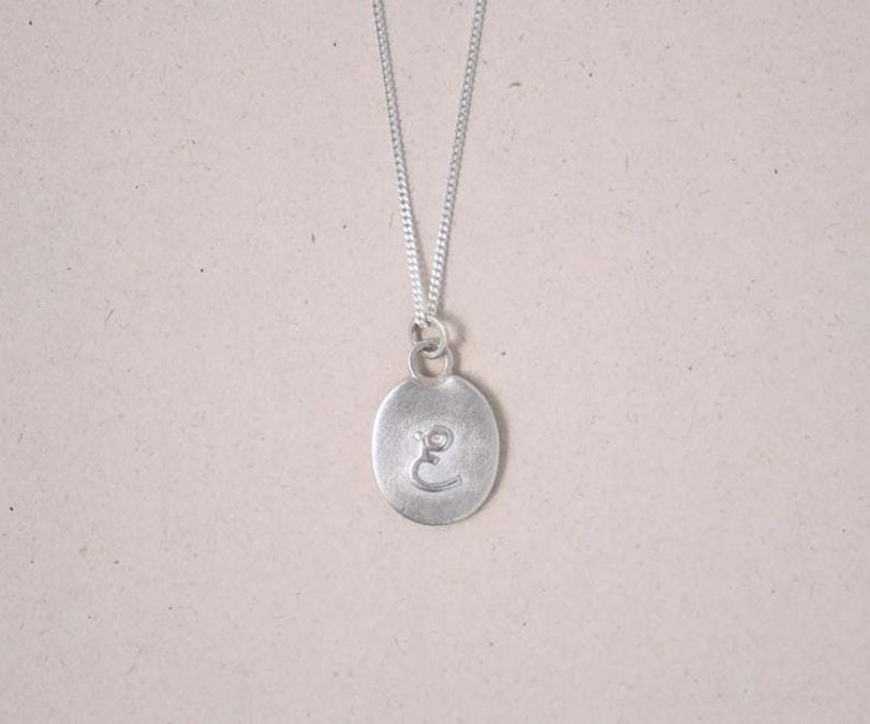 May include: A silver necklace with a round pendant featuring the letter "E" engraved on it.