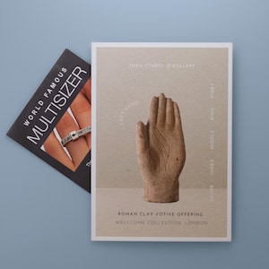 May include: A rectangular card featuring a beige background with a brown Roman clay votive offering of a hand, labeled with finger names and the text Thea Studio Jewellery and Wellcome Collection, London, next to a black World Famous Multisizer card.